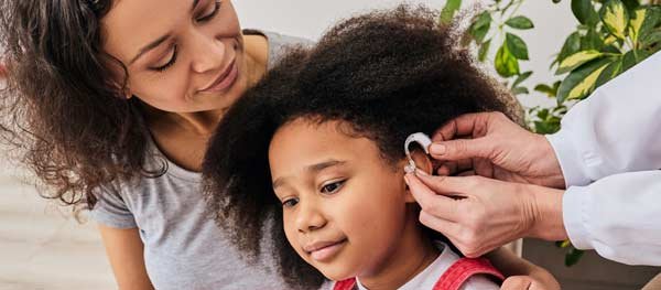 Mom with daughter who's having hearing aid put on