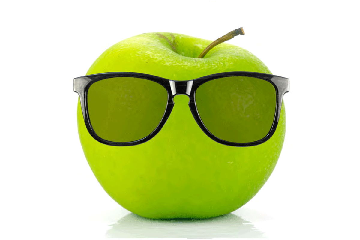 Green apple with sunglasses set on it.