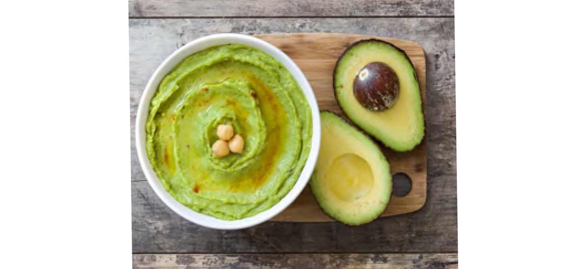 Bowl of avocado hummus with fresh avocado next to bowl