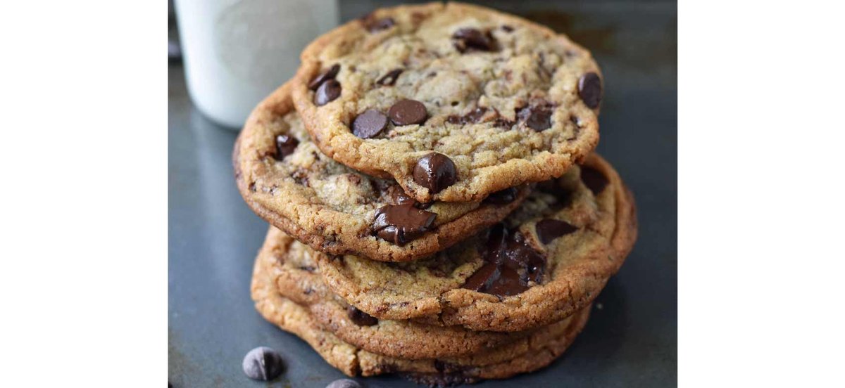 Stack of chocolate chip cookies with a glass of milk in the background