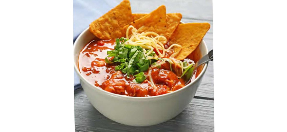 Bowl of turkey chili with tortilla chips and garnish