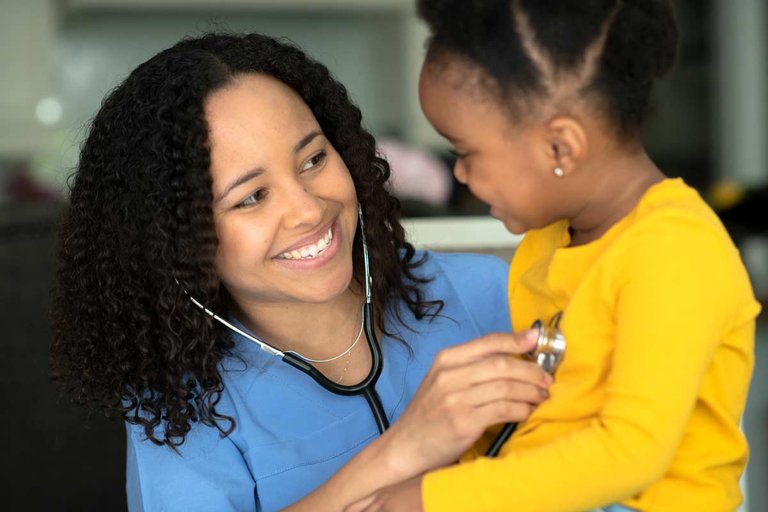 Smiling nurse checking young girl's heartbeat